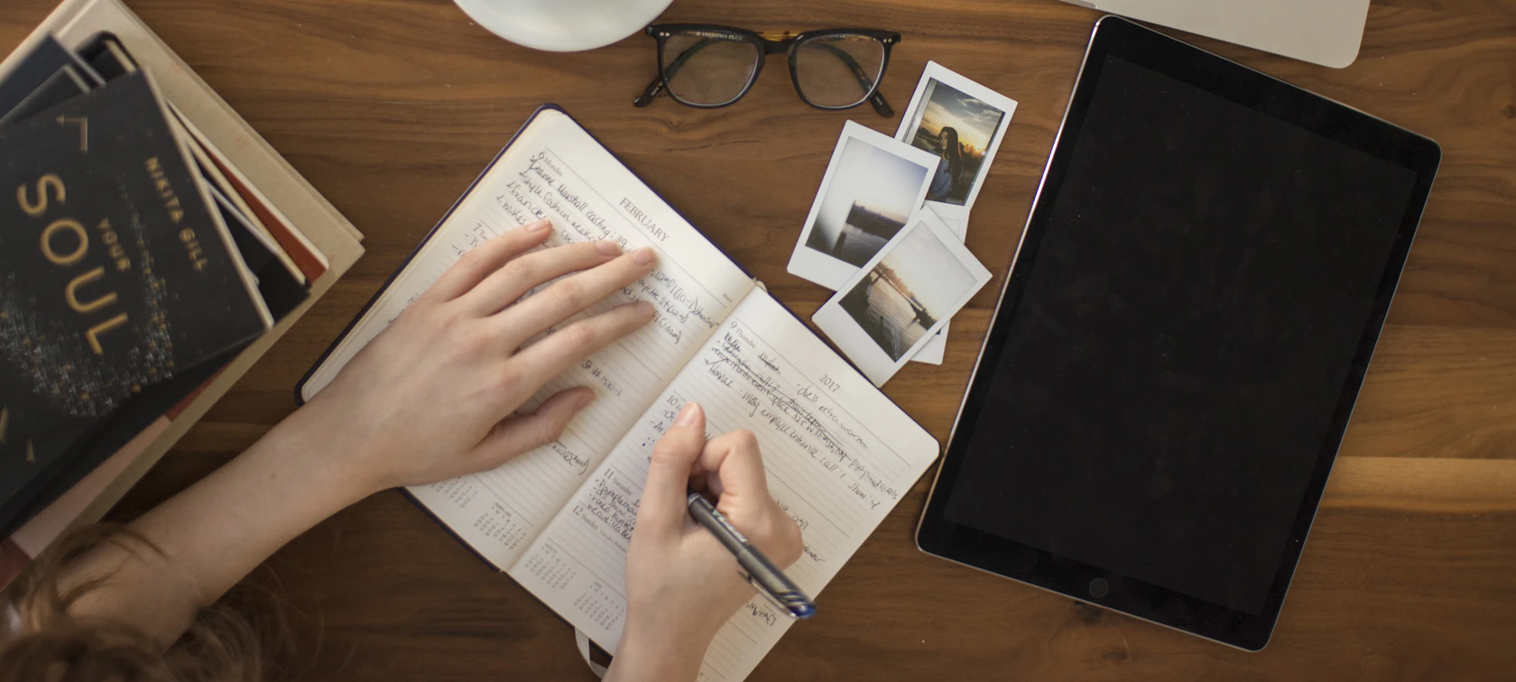 Writer taking notes in a notebook at a desk with a tablet and books