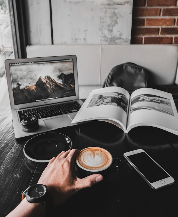 Writer holding a latte at a table with a laptop and magazine