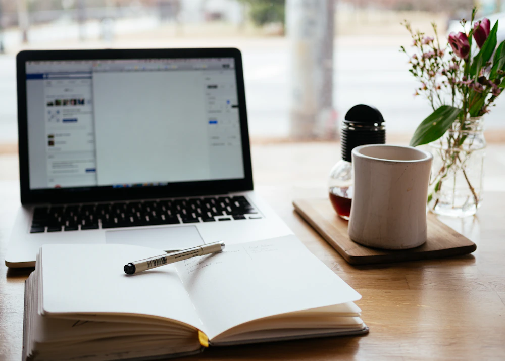 Laptop beside an open notebook and pen on a writing desk
