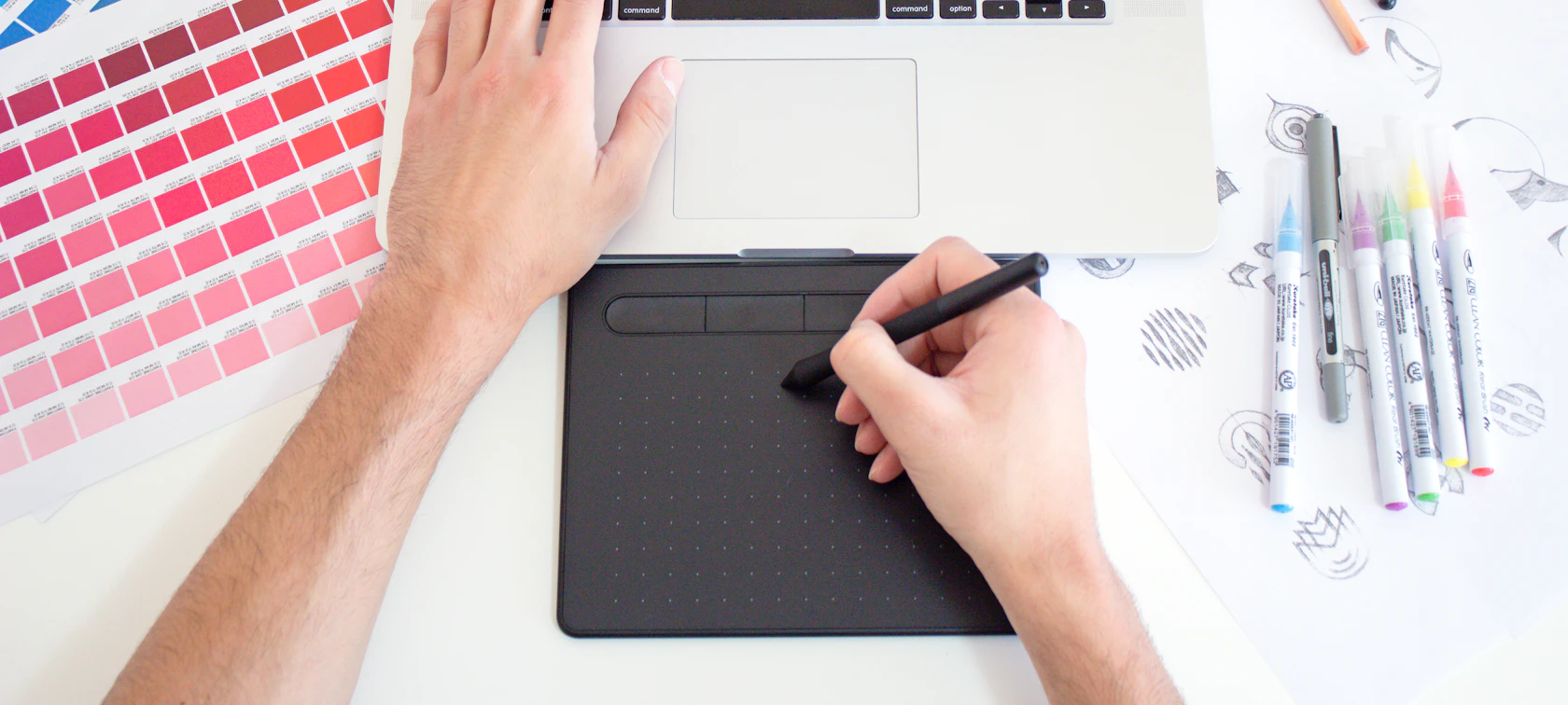 Graphic designer using a drawing tablet and laptop with color swatches