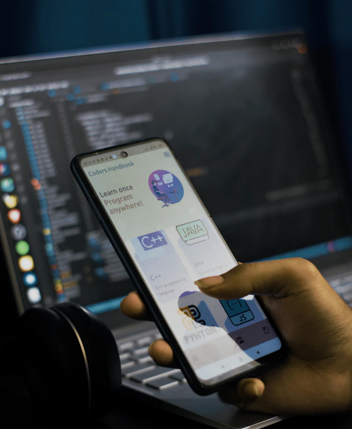 Developer testing a mobile app on a phone in front of code