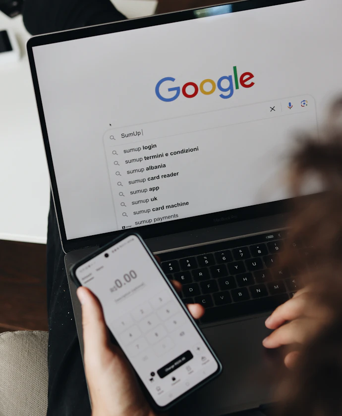 Person running a Google search on a phone and a laptop