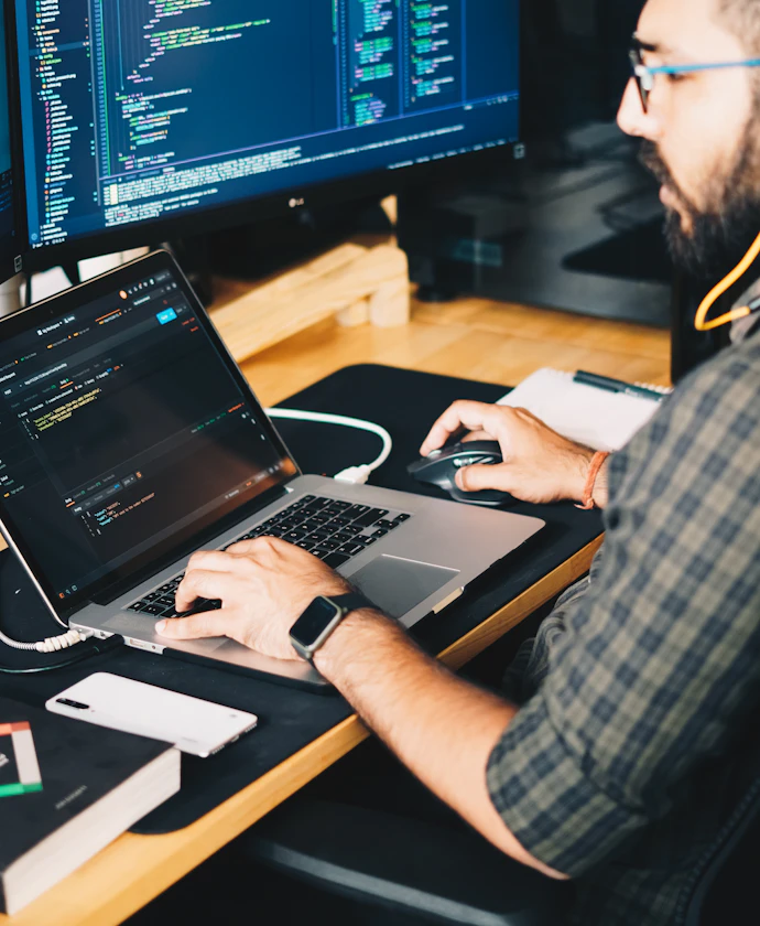 Software developer coding on a laptop with monitors of code