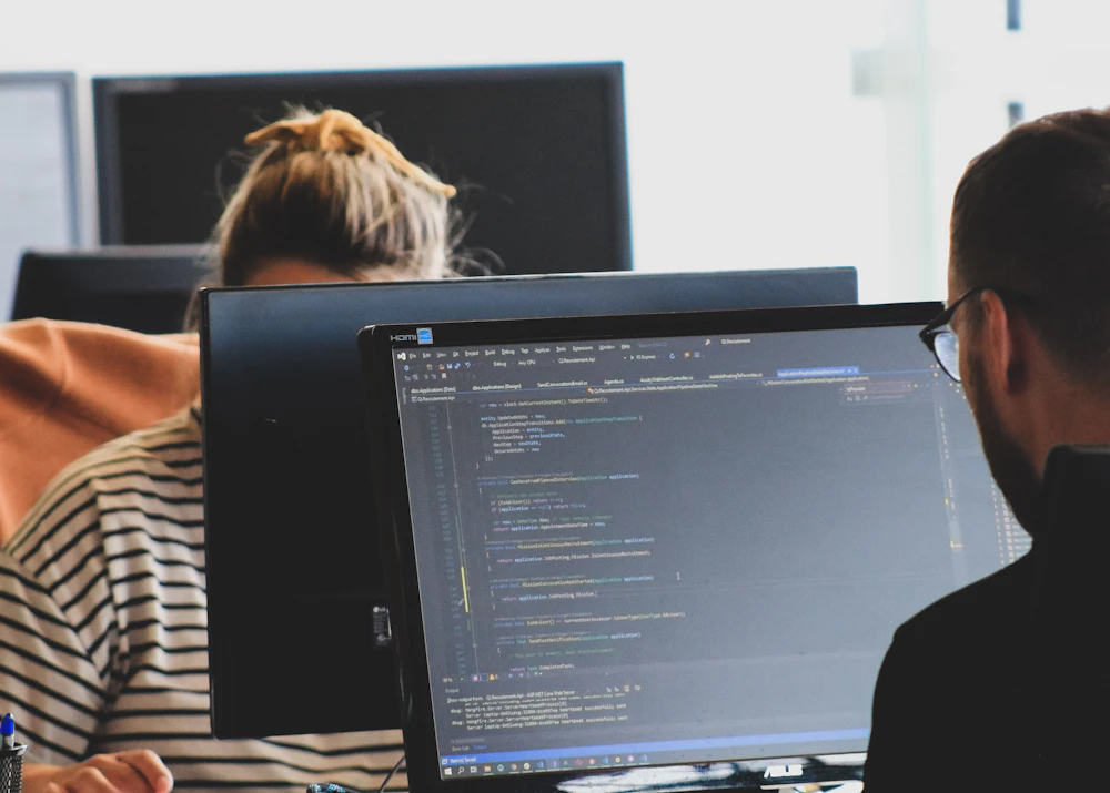 Two software developers reviewing code on monitors
