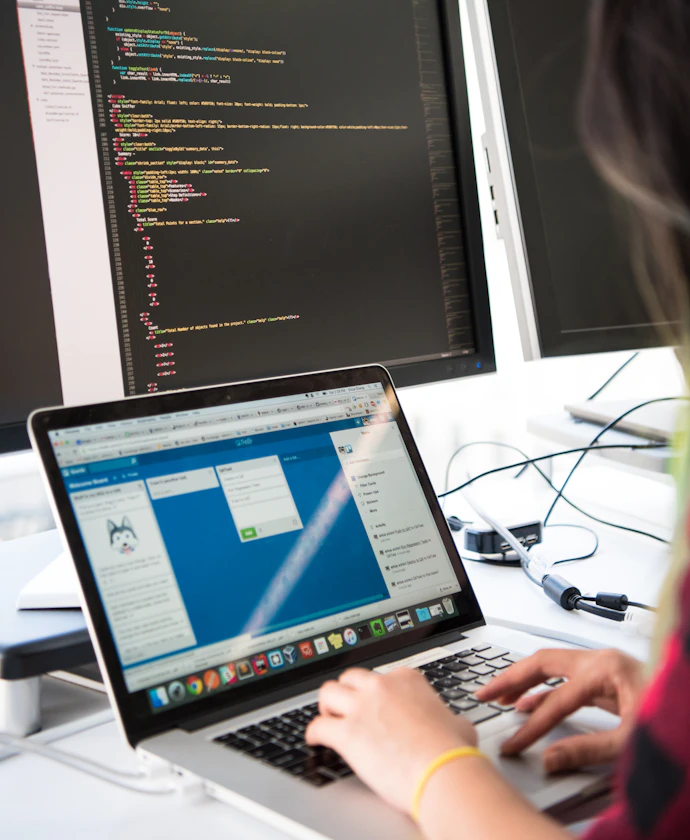Web developer working on a laptop beside a monitor of code